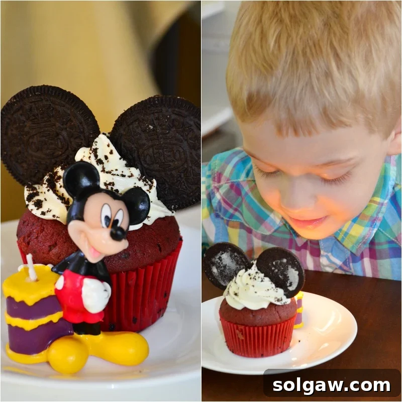 Two adorable Red Velvet Oreo Cupcakes, creatively decorated with fluffy white cream cheese frosting and whole Oreo cookies positioned as Mickey Mouse ears. A small Mickey Mouse themed birthday candle stands beside them on a vibrant, festive table.