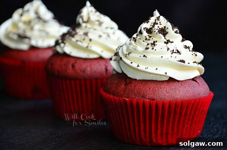 A beautifully decorated Red Velvet Oreo Cupcake, featuring a luxurious swirl of white cream cheese frosting and a generous dusting of crushed Oreo crumbs, perfectly centered and inviting against a soft, artistically blurred background.