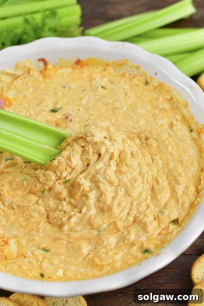 A serving of hot and bubbly Buffalo Chicken Dip with celery sticks for dipping.