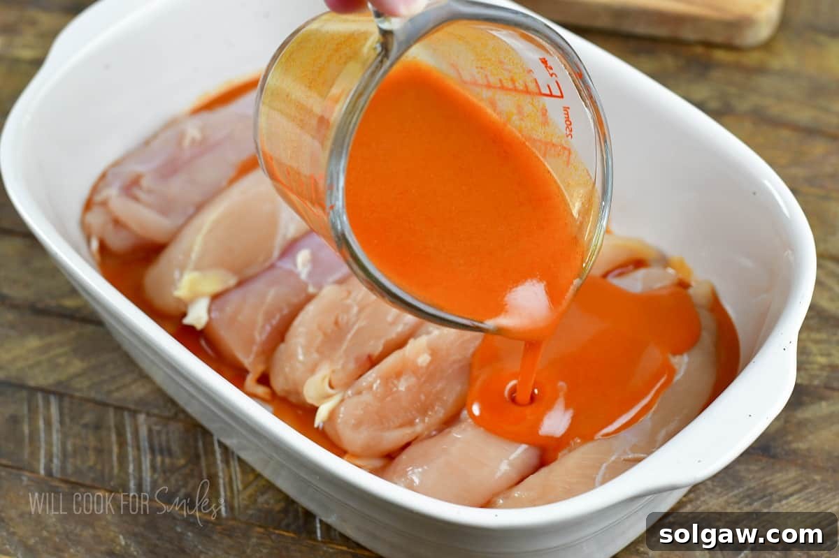 Adding buffalo wing sauce to raw chicken tenders in a baking dish before cooking.