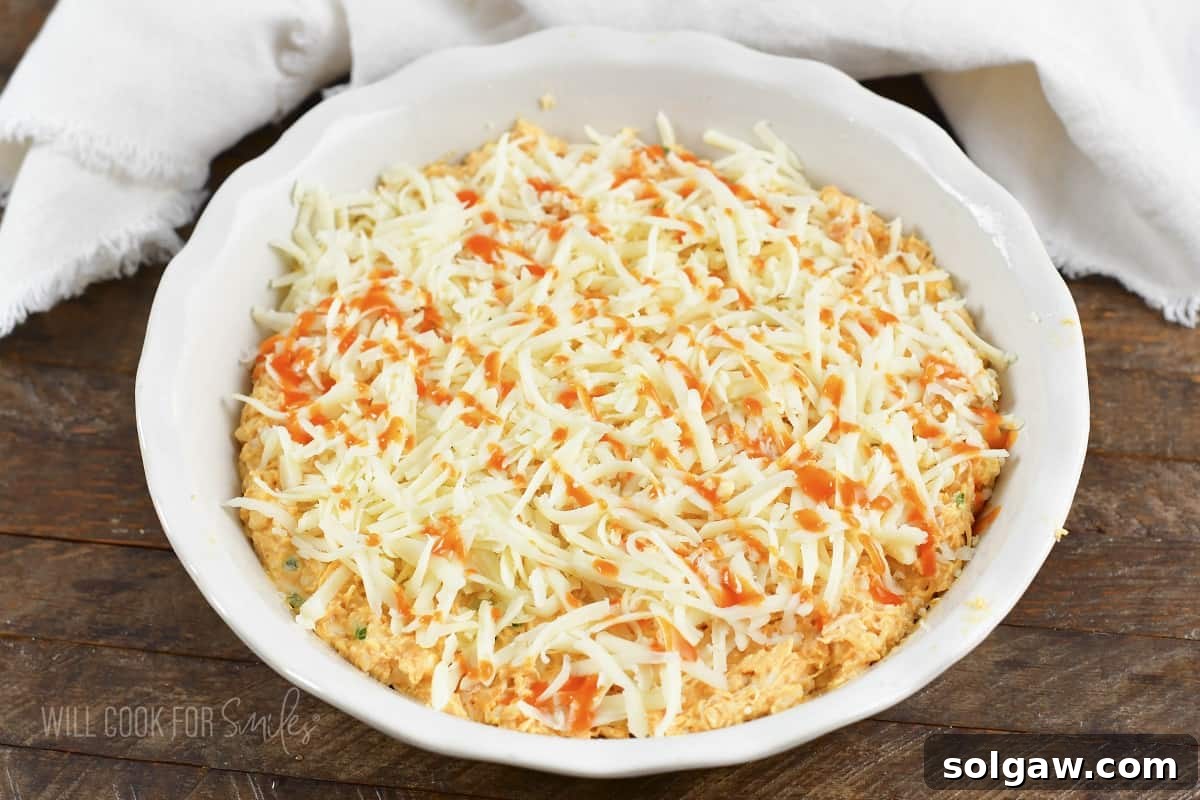 Close-up of shredded cheese and a drizzle of buffalo sauce on unbaked dip.