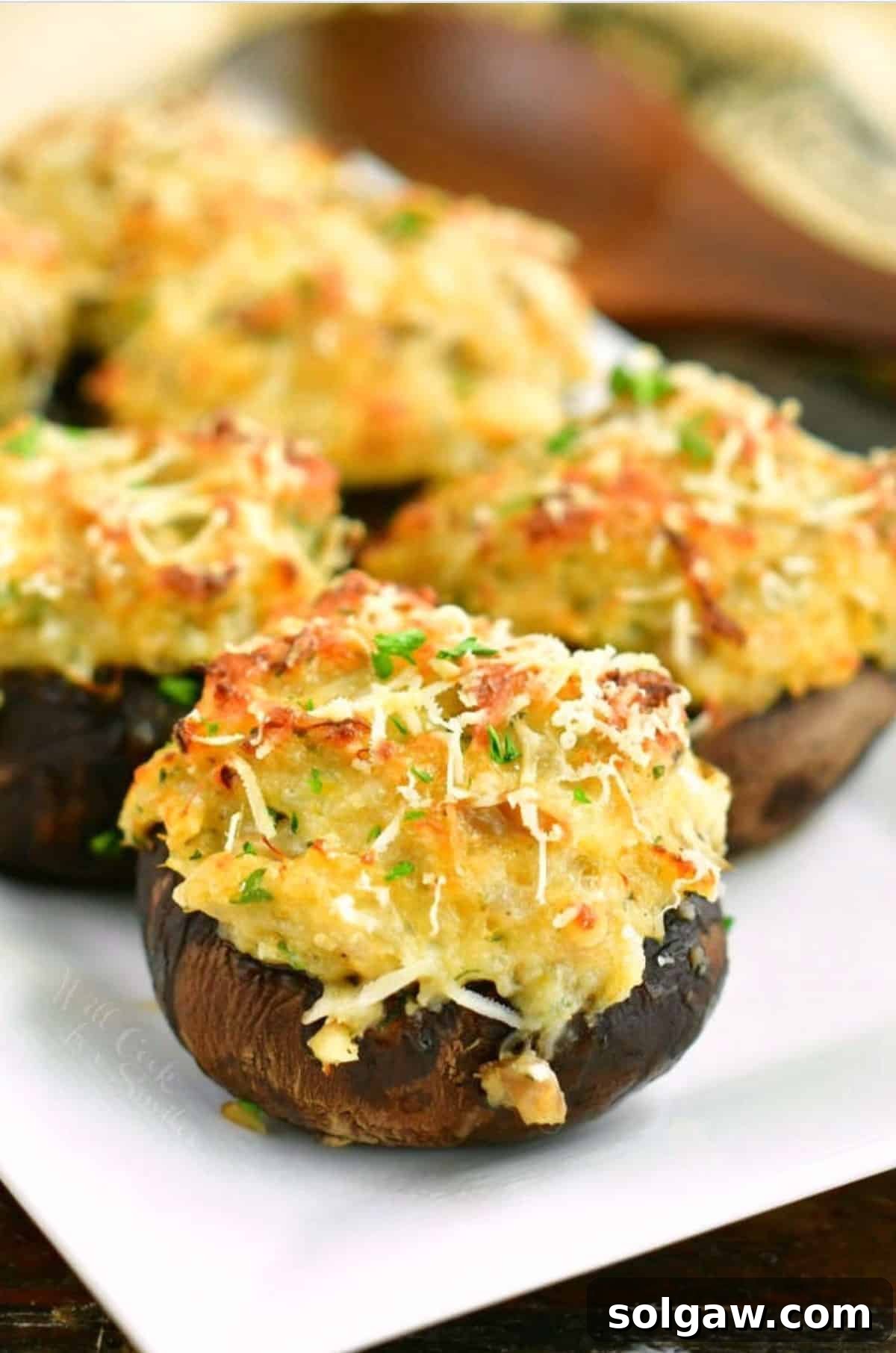 Crab stuffed mushrooms topped with golden panko and fresh herbs on a white platter.