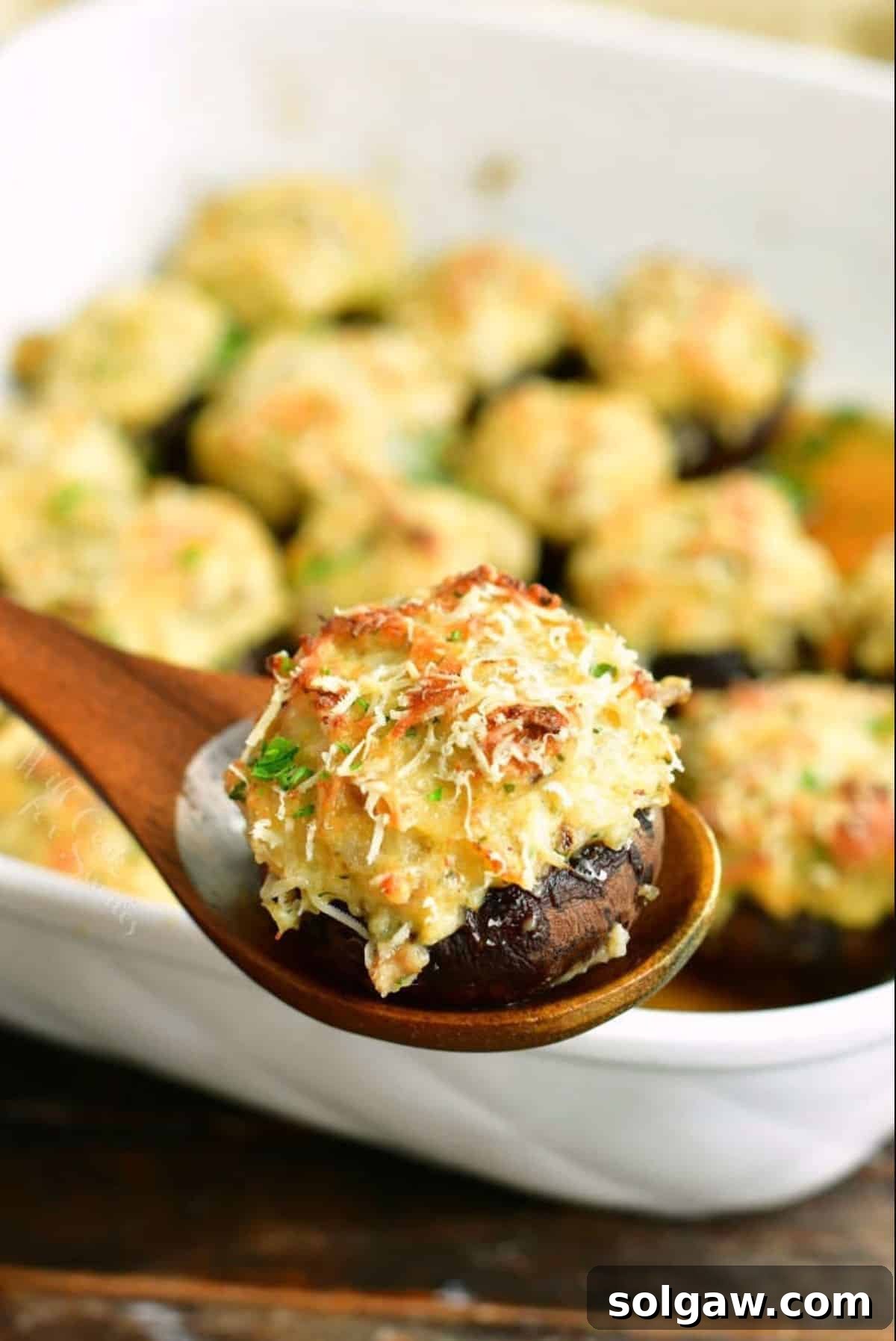 A perfectly baked crab stuffed mushroom being lifted from a white casserole dish, showcasing its golden-brown topping and tender cap.