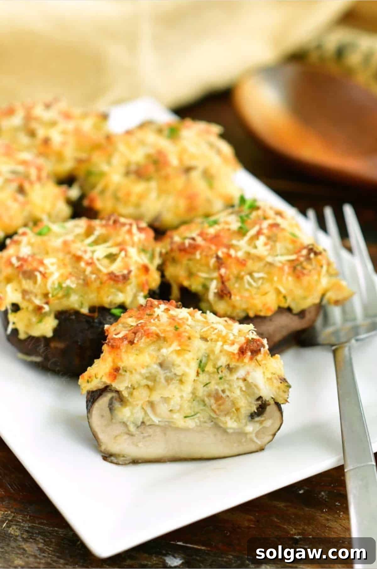 A plate of golden-brown crab stuffed mushrooms, with one mushroom cut in half to reveal the creamy filling, accompanied by a fork.
