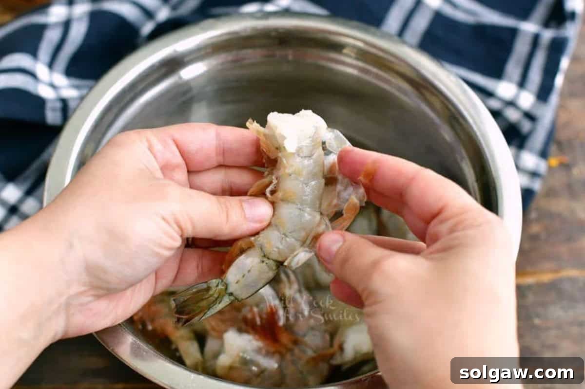 Close-up of a hand gently pulling the shell off a raw shrimp, exposing the meat.