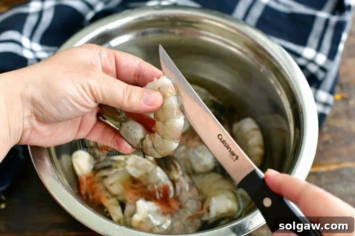 A close-up of a shrimp being deveined, with a paring knife gently slicing its back.