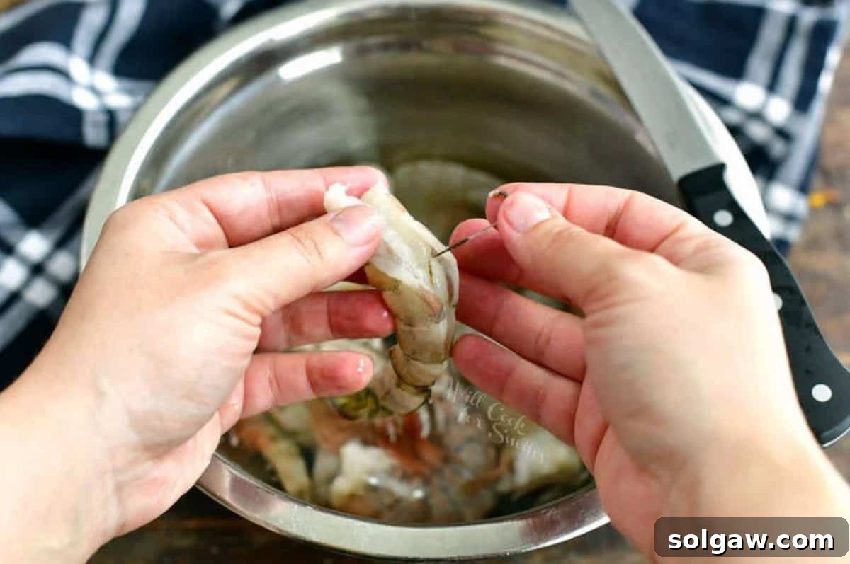 A hand gently pulling the dark vein out of a raw shrimp with the tip of a knife.