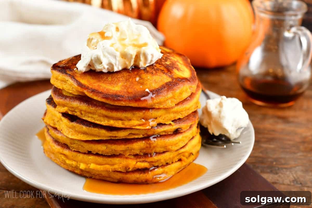 A beautiful stack of pumpkin pancakes, generously topped with whipped cream, inviting you to indulge.