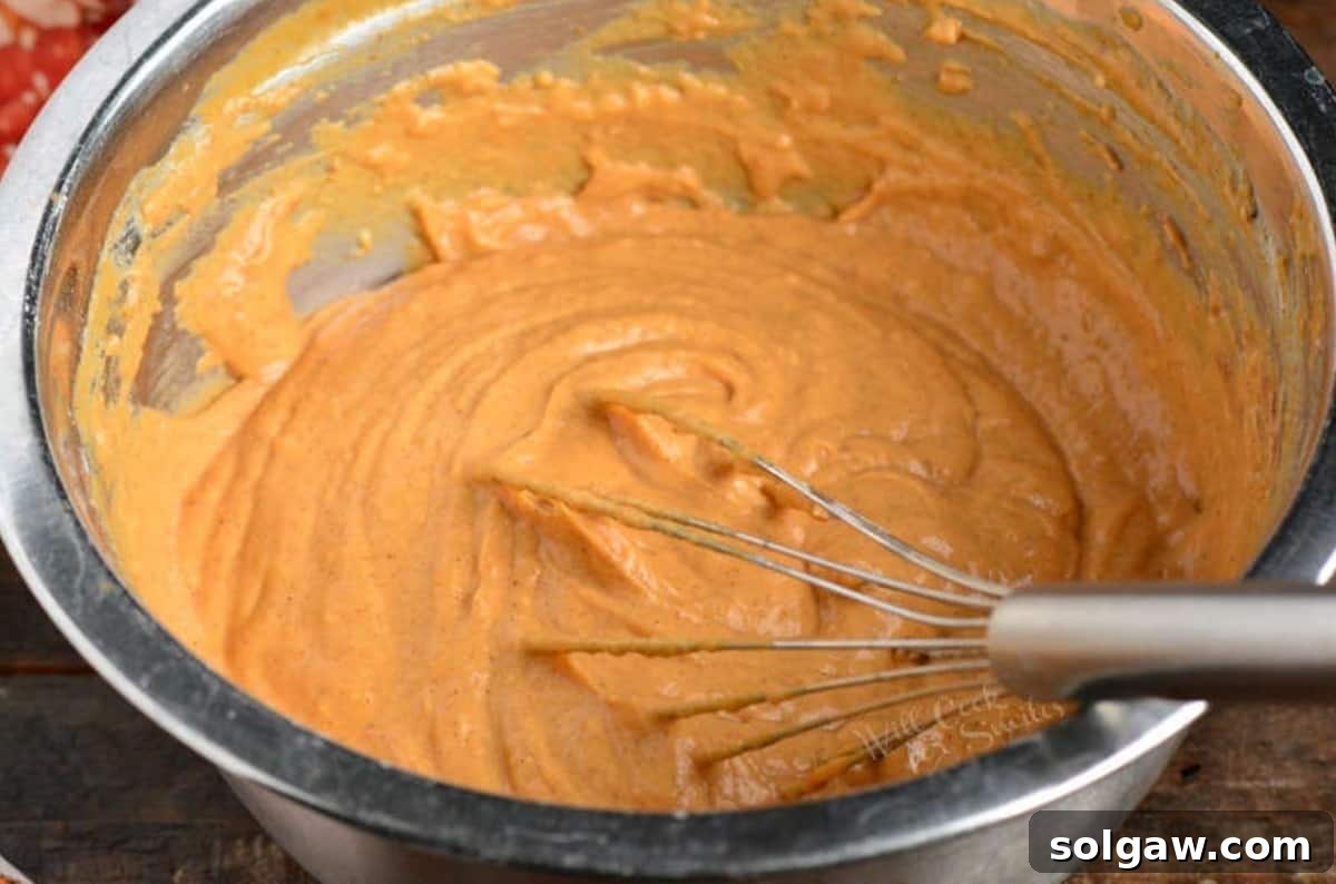 Pumpkin pancake batter is mixed smoothly in a bowl with a whisk, showing its perfect consistency.