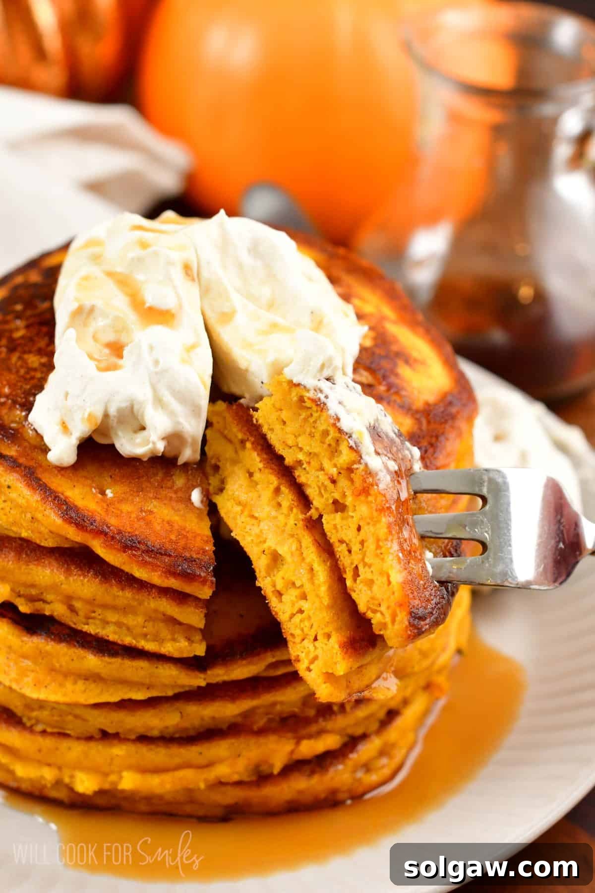 A fork taking a bite from a stack of pumpkin pancakes, showcasing the fluffy texture and rich toppings.