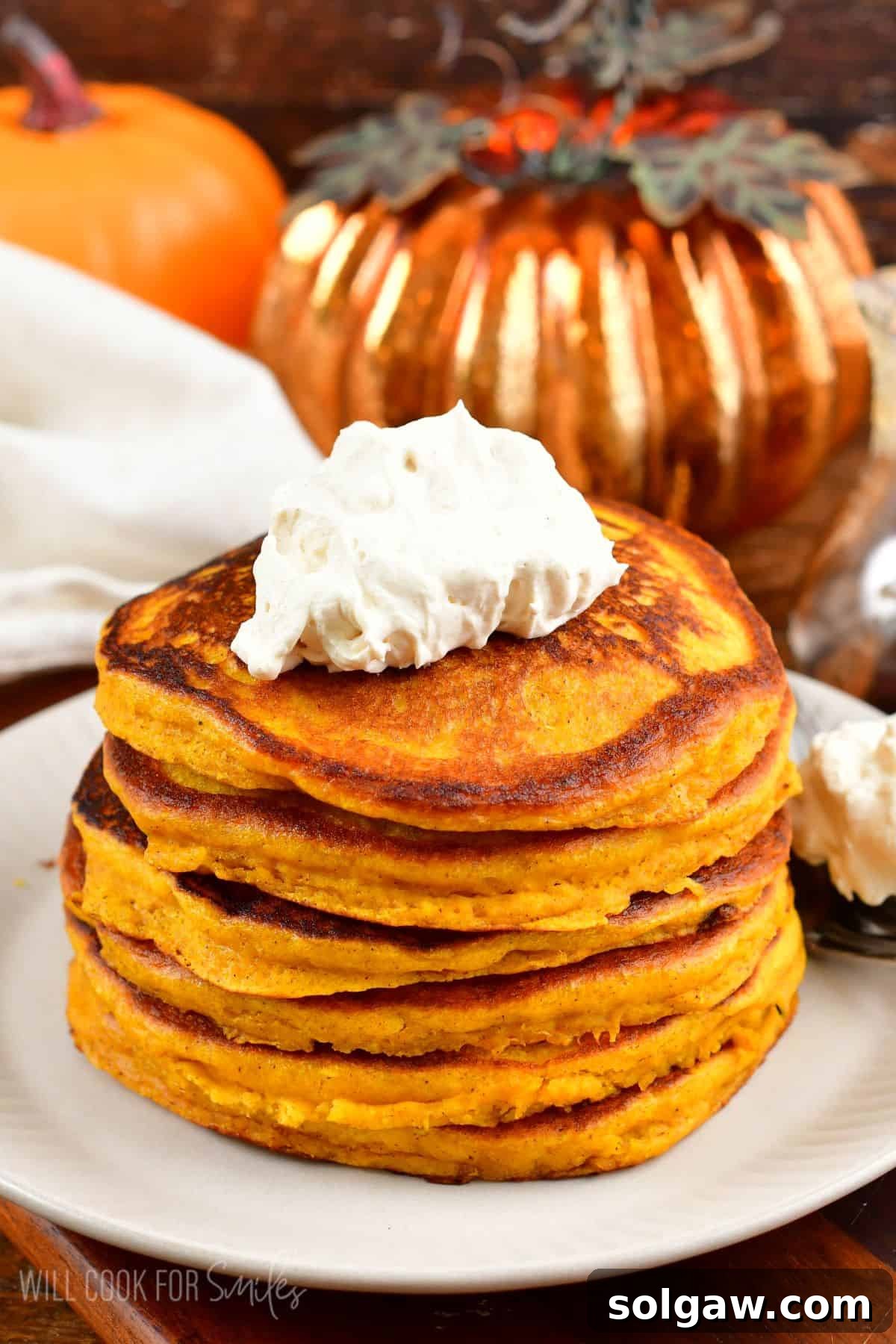 A vibrant stack of pumpkin pancakes, beautifully presented with a dollop of whipped cream on top, ready to be enjoyed.