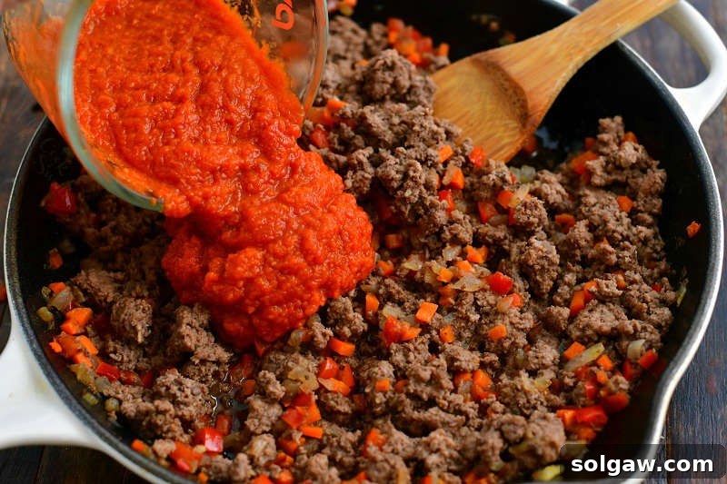 Hearty Italian Beef Stuffed Zucchini 4 pouring in red tomato sauce into the cooked beef and vegetable mixture in a skillet