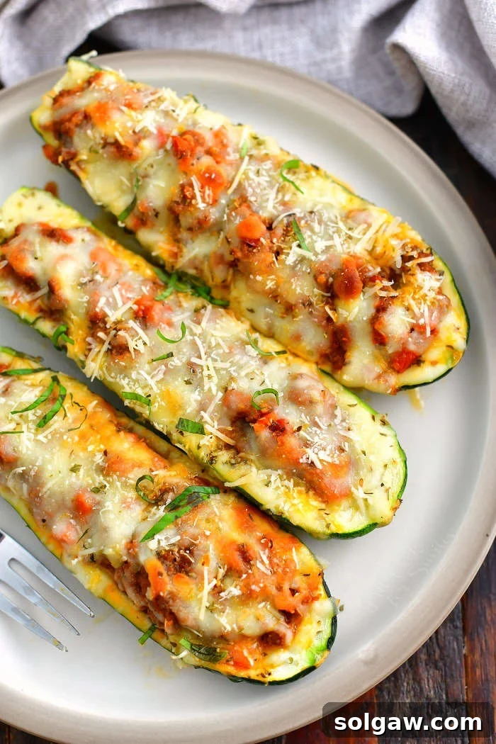Hearty Italian Beef Stuffed Zucchini 7 three stuffed baked zucchini boats side by side on a light tan dish with a grey towel next to it
