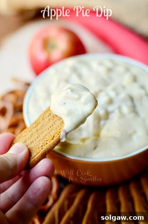 Warm Apple Pie Dip served in a brown bowl, with a cookie scooping some of the creamy, spiced dip