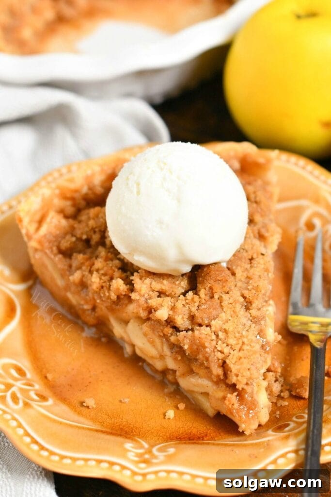 Slice of Dutch apple pie with scoop of vanilla ice cream on a brown plate, ready to be enjoyed