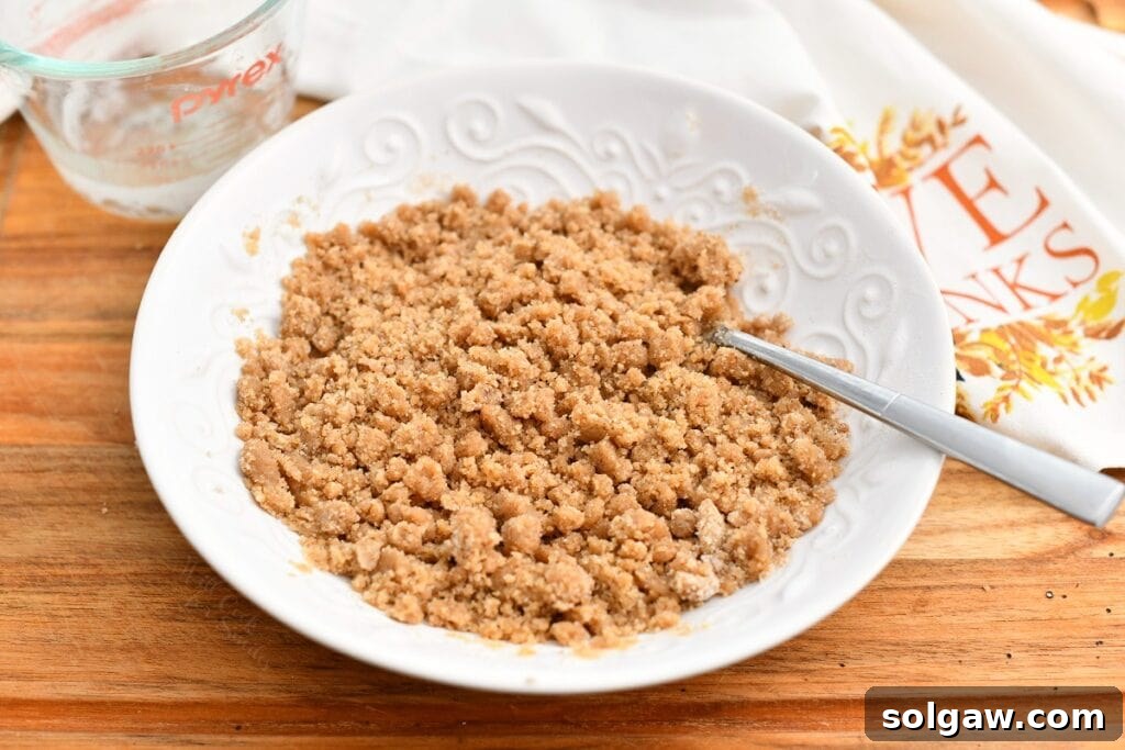 Brown sugar crumble topping in white bowl with spoon, showing perfect crumbly texture