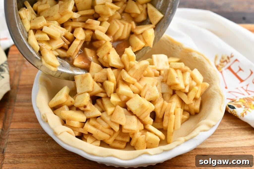 Pouring spiced apple mixture into unbaked pie crust