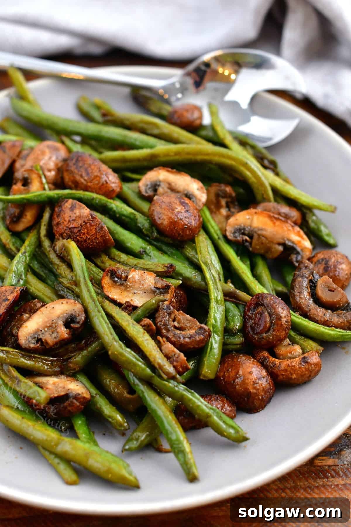 Savory Mushroom and Green Bean Roast 8 A beautifully presented bowl of roasted green beans and mushrooms with a serving spoon.