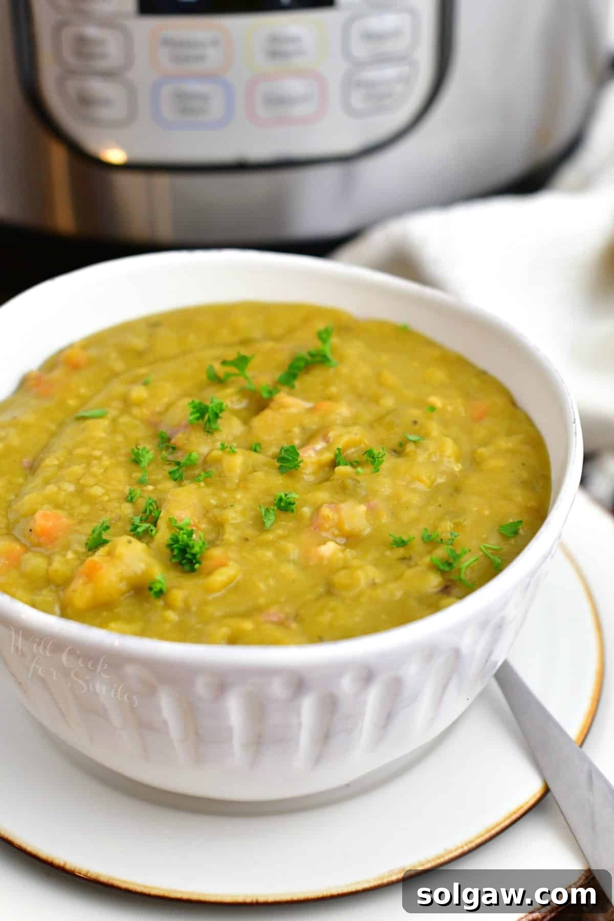 thick hearty split pea soup in white bowl with spoon on a plate.