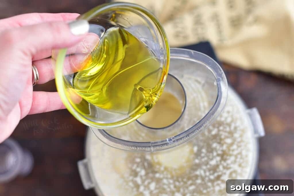 Slowly pouring olive oil into a food processor to emulsify the homemade Caesar dressing