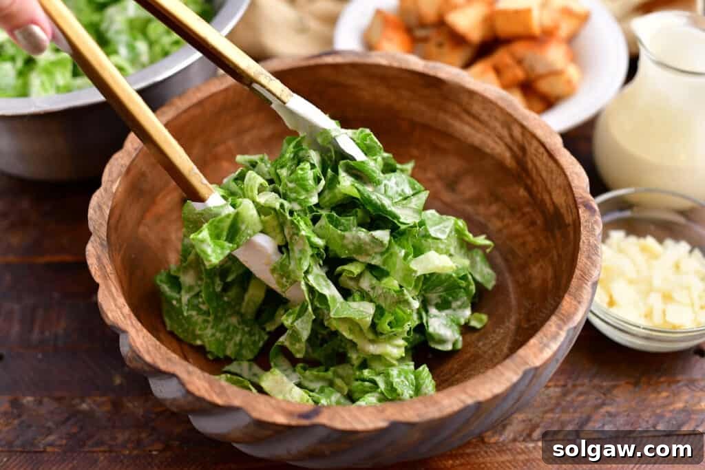Serving a generous portion of freshly tossed Caesar salad into a smaller bowl using tongs