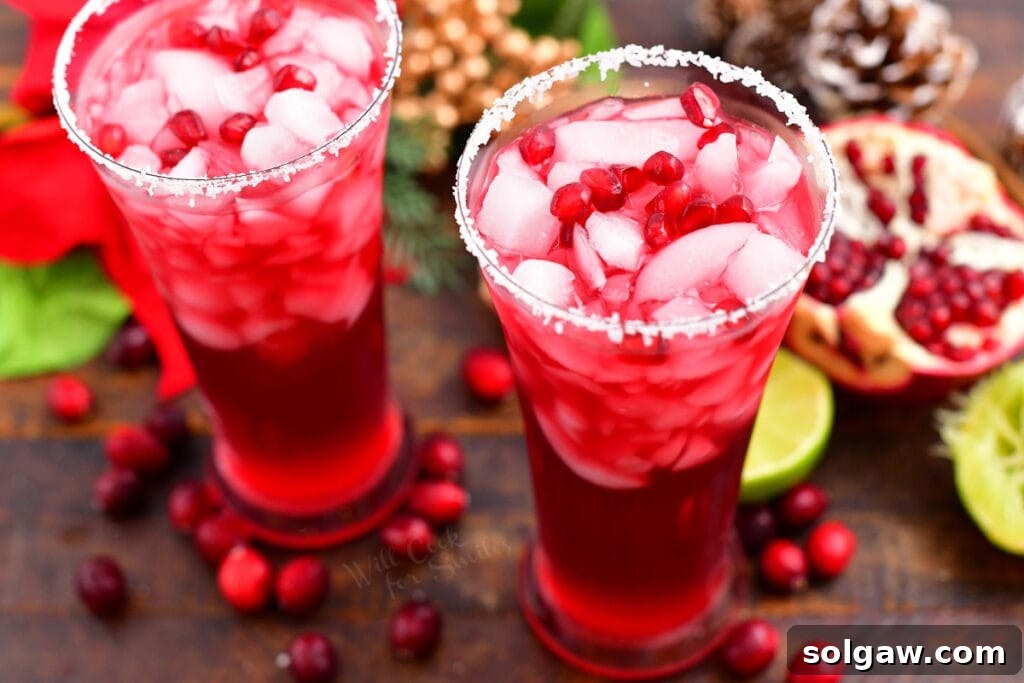 Two full glasses side by side filled with bright red margarita cocktail garnished with lime