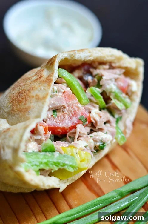Coastal Tuna Pita with Bright Herb Aioli 7 A freshly made Greek Tuna Pita, sliced in half, showcasing its vibrant filling, resting elegantly on a wooden cutting board