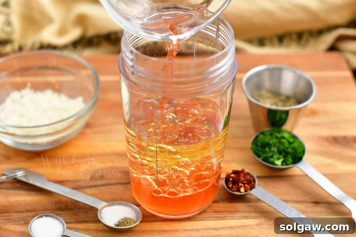 Zesty Italian Vinaigrette 5 pouring red wine vinegar into mason jar with oil, beginning the dressing process.