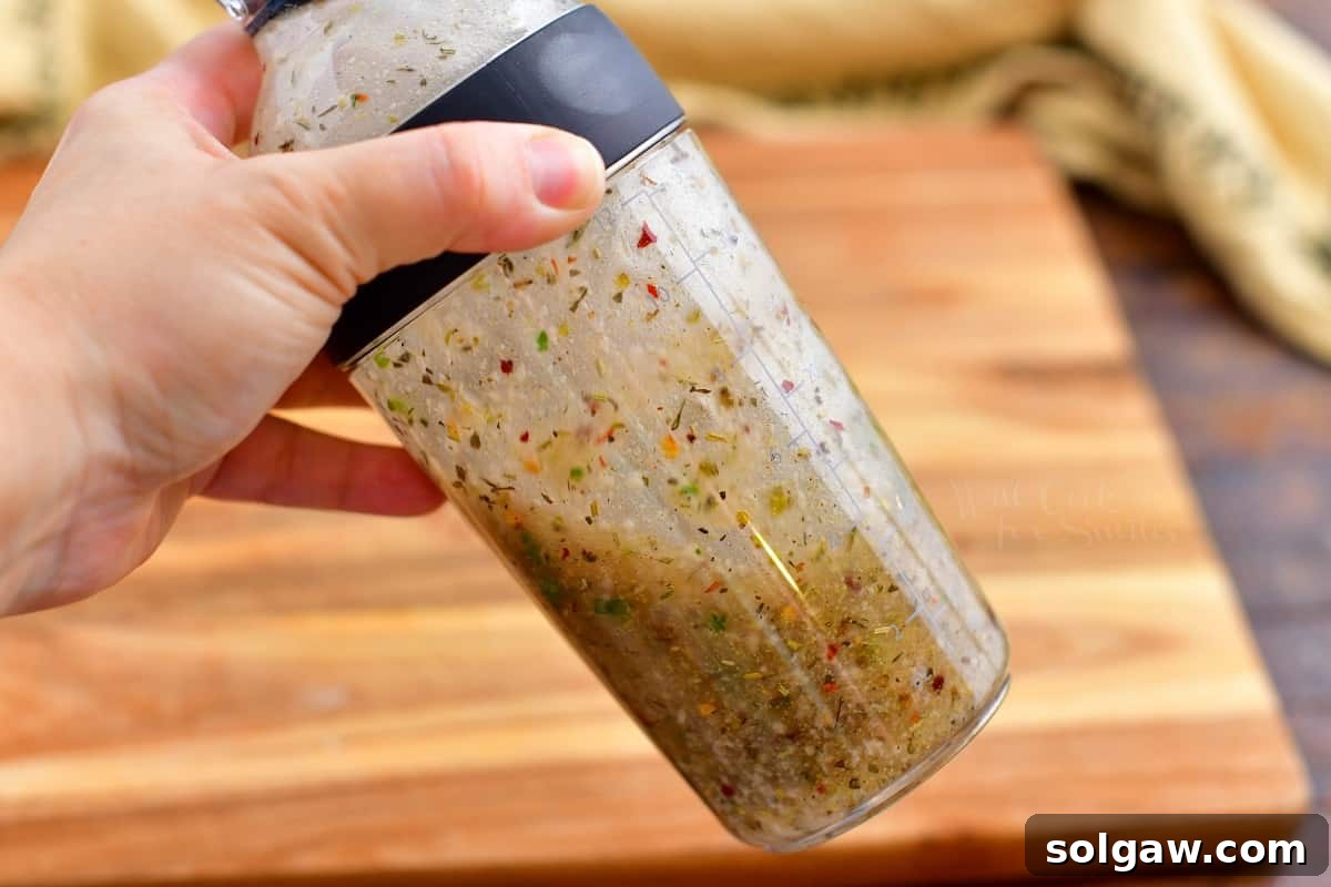 Zesty Italian Vinaigrette 7 creating an emulsion with oil, vinegar, herbs and spices in shaker glass, showing the creamy texture.