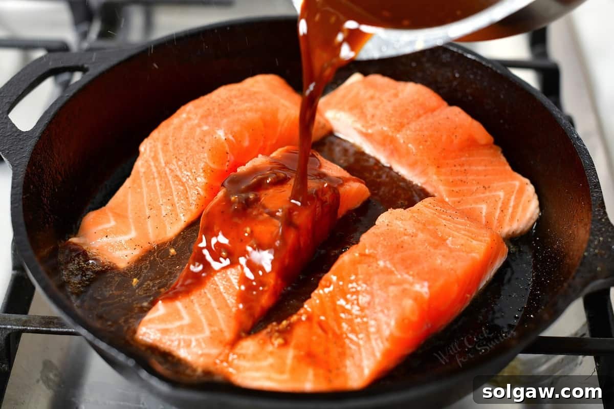 Sticky Sweet Teriyaki Salmon 5 teriyaki sauce being poured over salmon fillets in a cast iron skillet