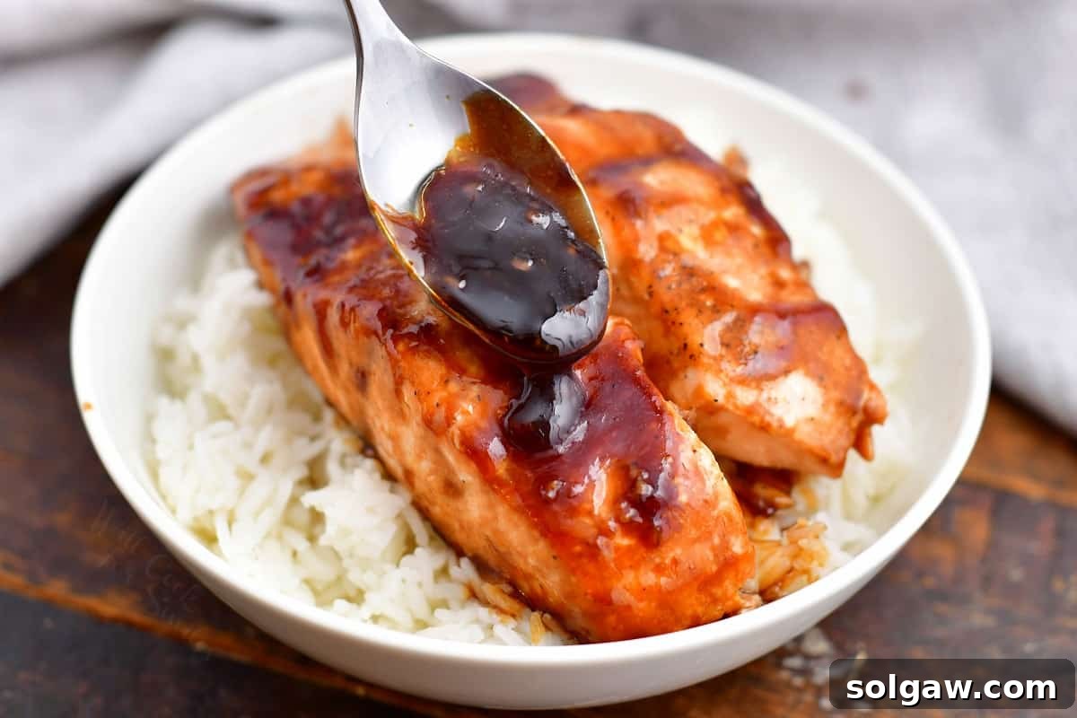 Sticky Sweet Teriyaki Salmon 6 spooning sauce onto teriyaki salmon in white dish on bed of jasmine rice