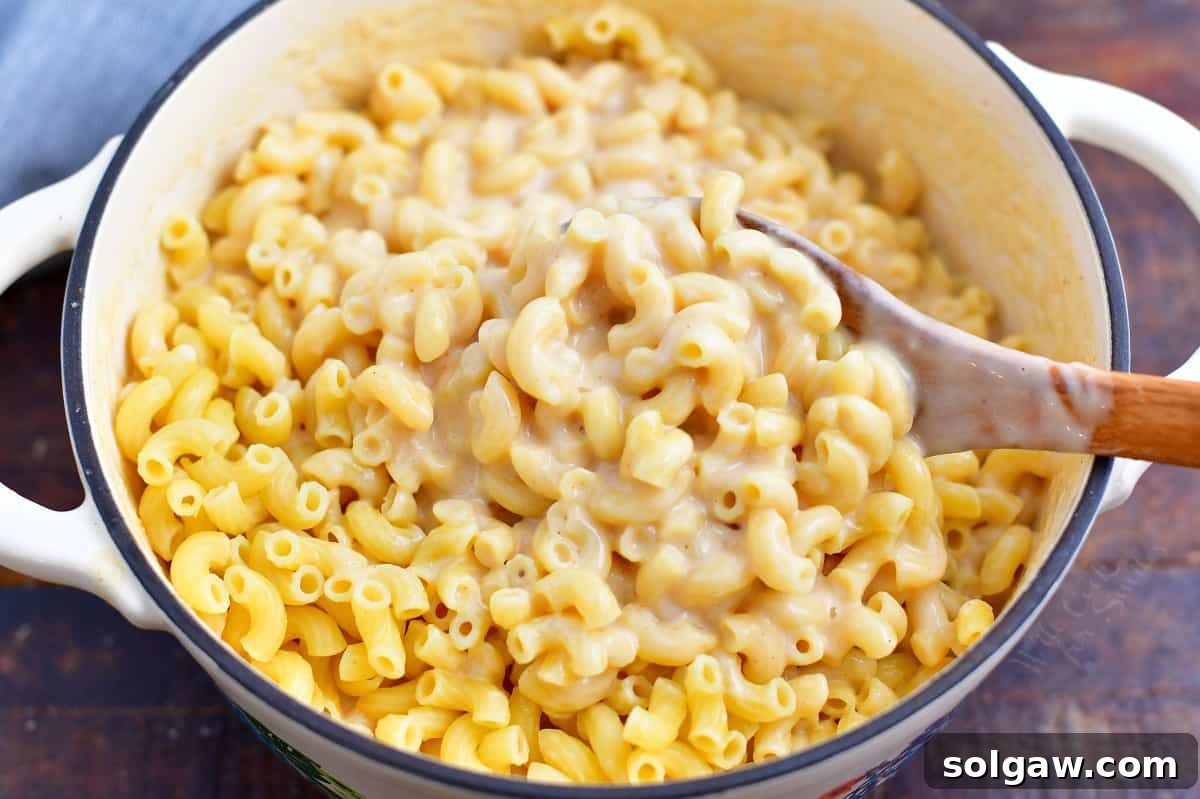 Craft Beer Mac and Cheese 7 wooden spoon stirring sauce into a pot of elbow pasta