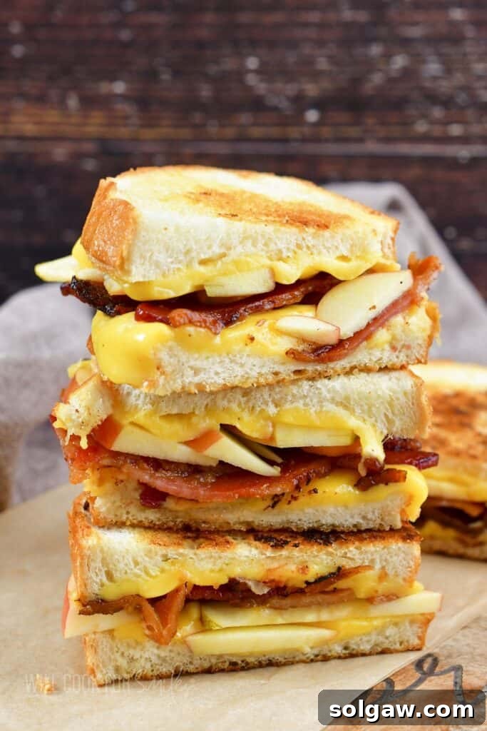 Side view of three apple bacon grilled cheese halves stacked, showing layers of melted cheese, bacon, and apple.