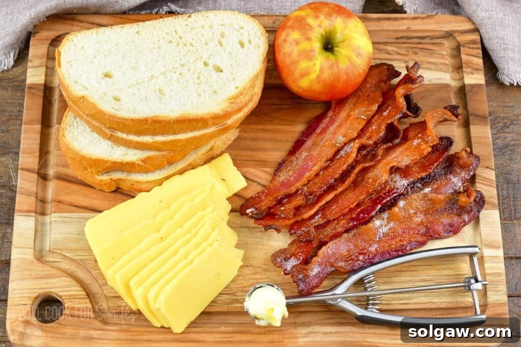 Ingredients to make bacon apple gouda grilled cheese laid out on a wooden board: bread, bacon, cheese, apple, and butter.