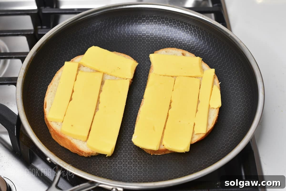 Two slices of sourdough bread topped with shredded Gouda cheese in a pan, ready for the next layer.