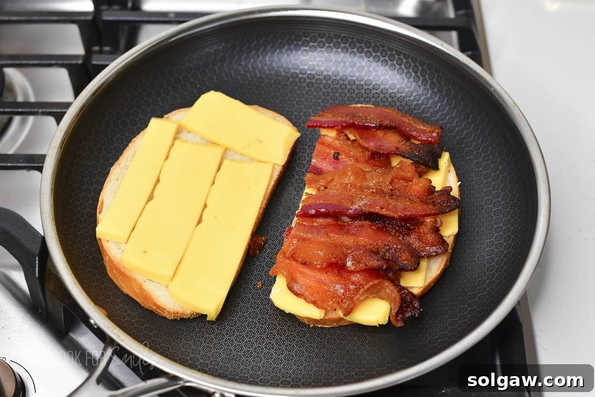One slice of bread in the pan with cheese and the other with cooked bacon on top of the cheese.