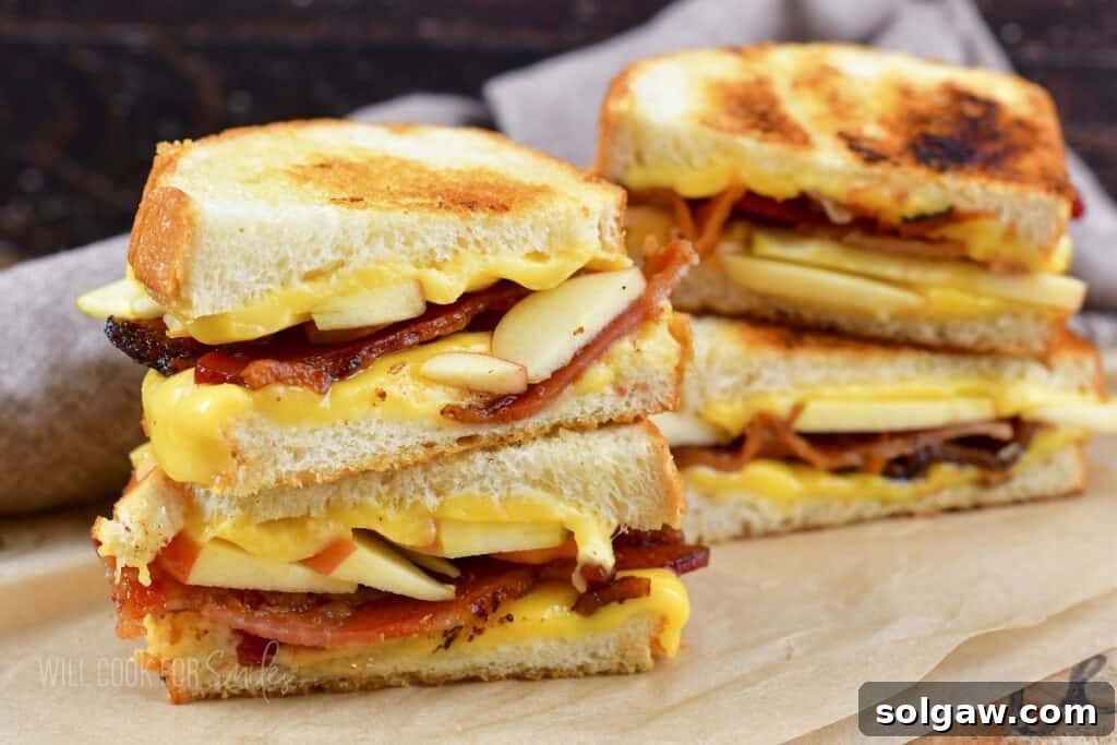 Close-up of two stacked bacon and apple grilled cheeses, showing melted cheese and crisp ingredients.