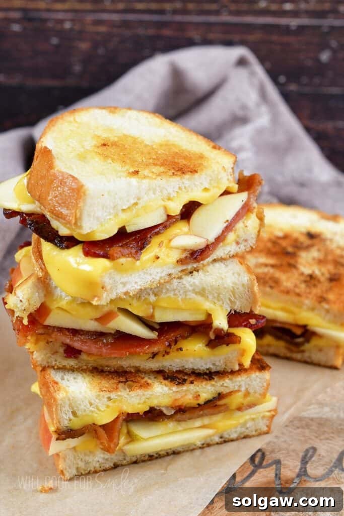 Three bacon apple grilled cheese halves stacked on a wooden board.
