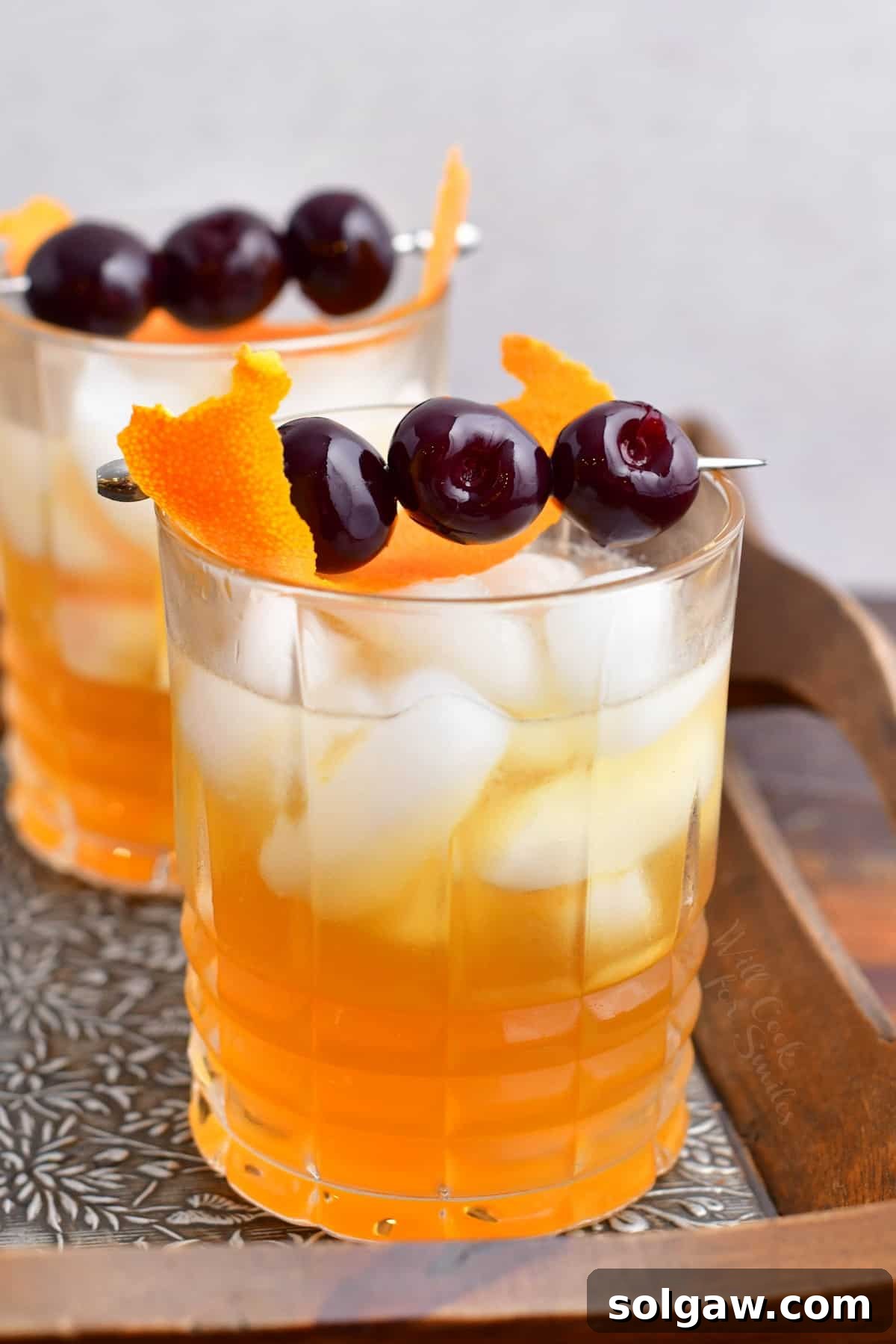 Two glasses of Amaretto Sour cocktail are ready to be enjoyed, garnished with orange peels and cherries.