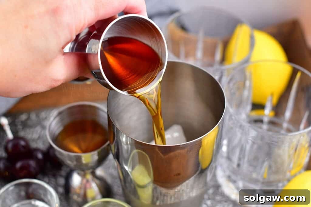 Velvet Almond Sour 4 A dark liquor, likely amaretto, is being poured into a metal cocktail shaker already containing ice.