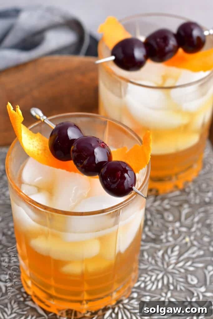 Velvet Almond Sour 10 Two glasses filled with ice and Amaretto Sour cocktail are presented on a metal surface, showcasing the vibrant color and garnishes.