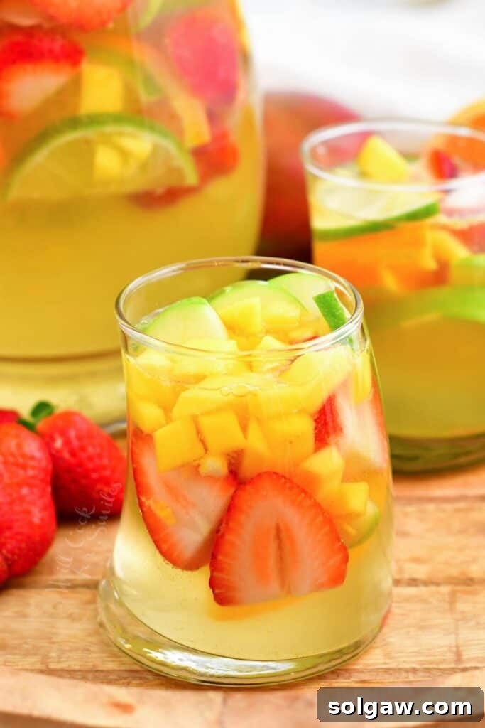 Summer's Perfect White Sangria 2 Two glasses of white sangria are placed next to a full pitcher, garnished with fresh fruit.