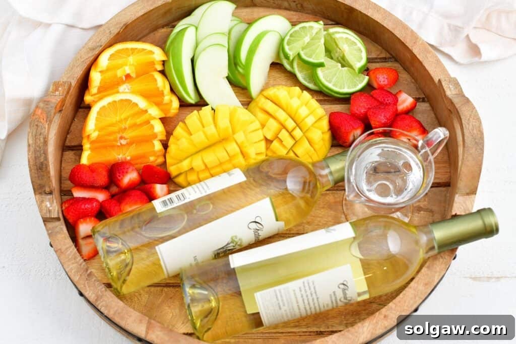 Summer's Perfect White Sangria 3 A selection of fresh fruits including oranges, limes, apples, strawberries, and mangoes, along with a bottle of white wine and Cointreau, are arranged on a circular surface, ready for making white sangria.