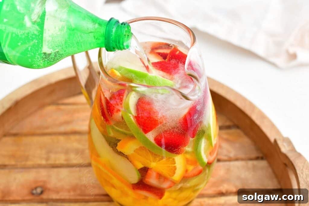 Summer's Perfect White Sangria 5 A stream of lemon-lime soda is being poured from a can into a large pitcher of chilled white sangria, adding fizz and a final touch.