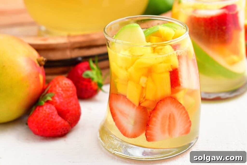Summer's Perfect White Sangria 7 A close-up of a glass of white sangria brimming with colorful strawberries and mangoes, showcasing the fresh fruit content.
