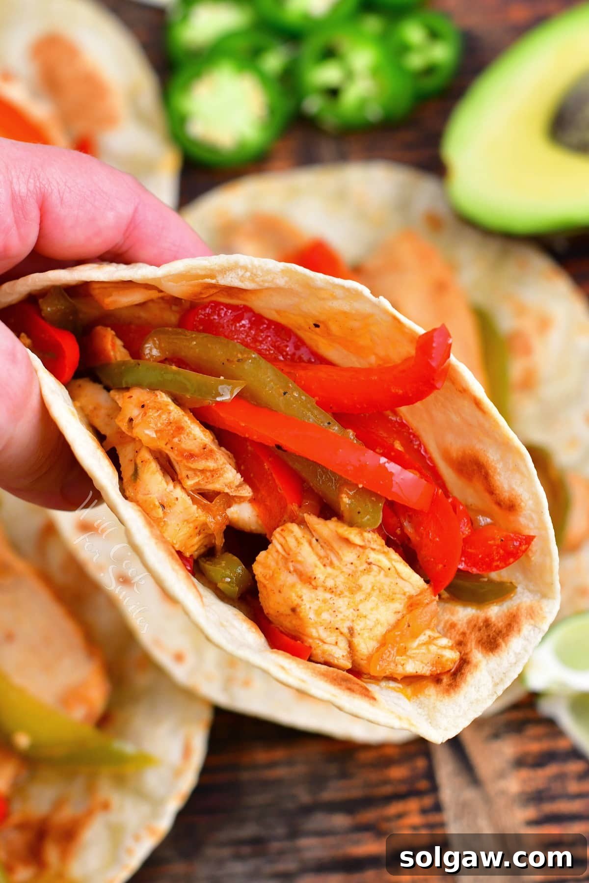 Sizzling Chicken Fajitas 10 A hand holding a perfectly assembled chicken fajita, showcasing the vibrant chicken and vegetables.