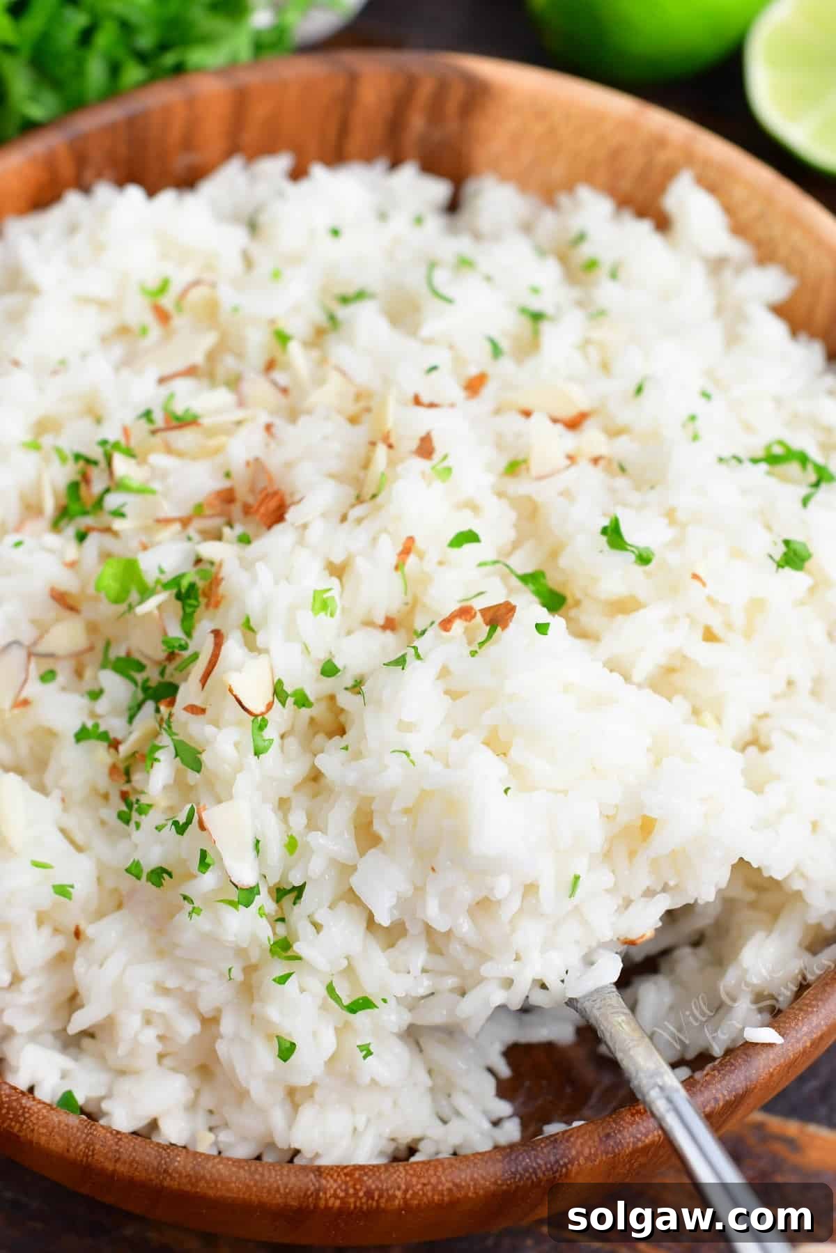 Fragrant Coconut Rice 2 A large wooden bowl is filled with coconut rice, garnished with fresh herbs and toasted almonds.