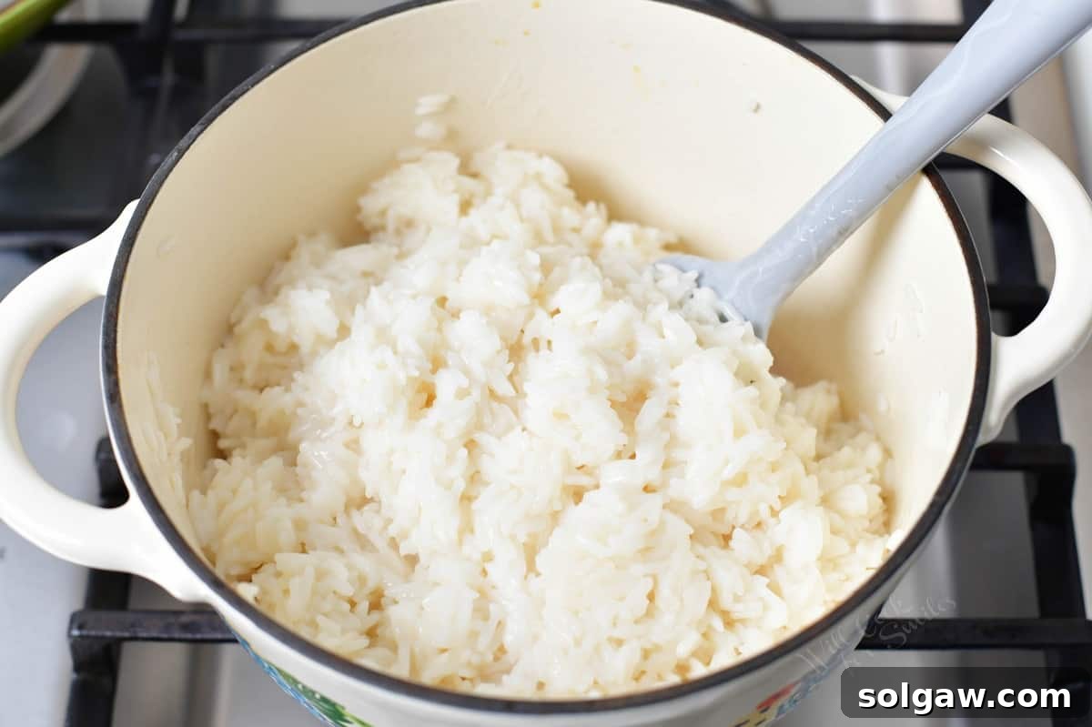 Fragrant Coconut Rice 6 Fluffy coconut rice is shown in a pot, being gently fluffed with a spatula, highlighting plump and separate grains.