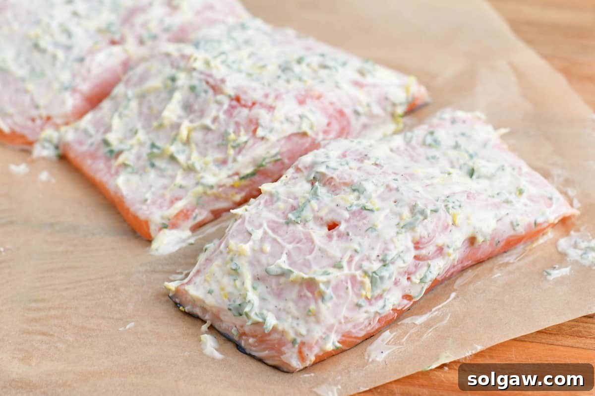 Salmon fillets are evenly covered with a fresh mayonnaise mixture on a parchment-lined baking sheet, ready for the next step.
