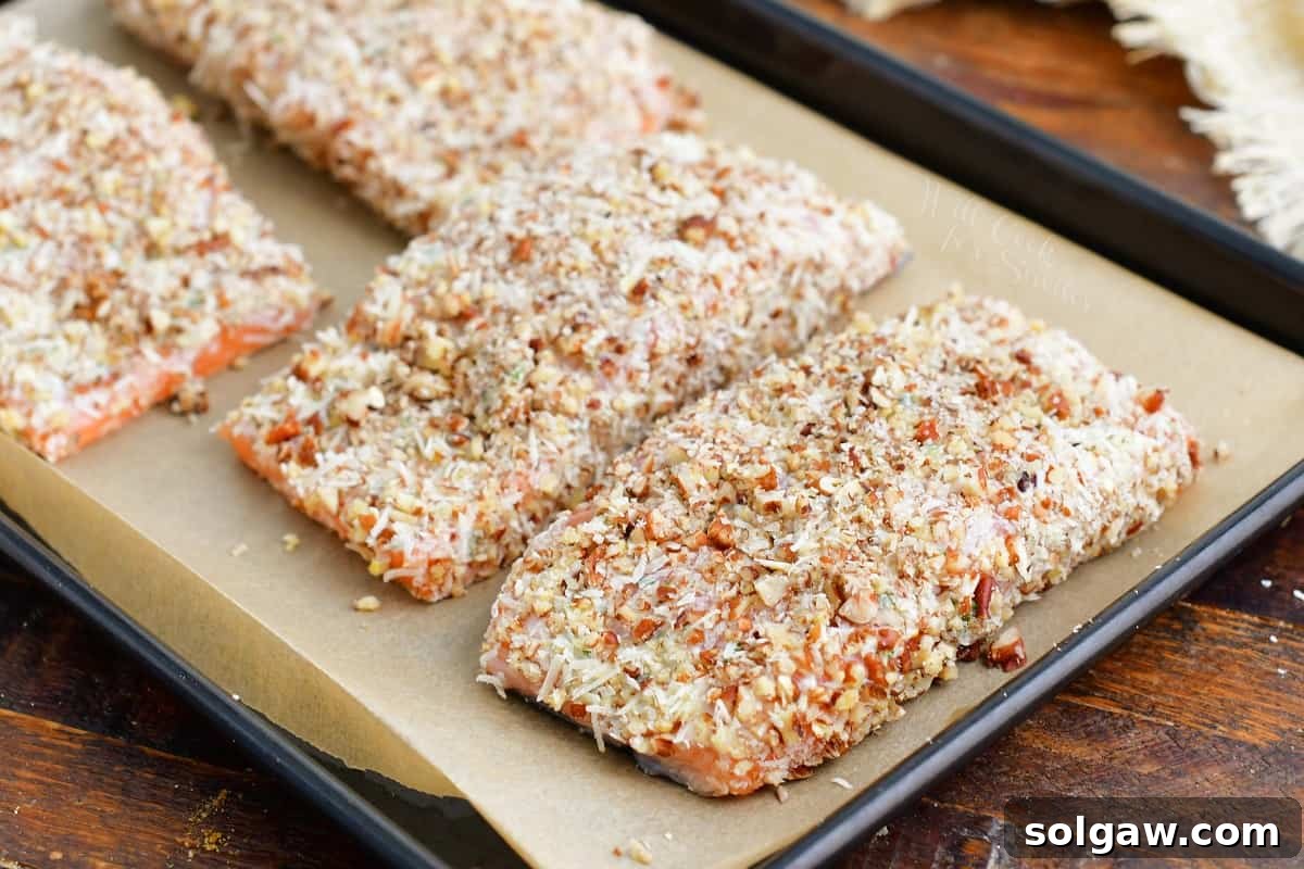 Pecan crusted salmon fillets, uncooked and perfectly coated, are arranged on a baking sheet, ready for the oven.